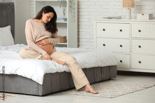 Pregnancy discomfort and swollen feet, pregnant woman sitting on bed feeling ...