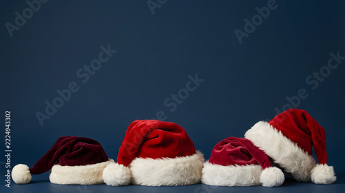Row of red velvet santa claus hats for christmas holiday celebration isolated on dark blue background