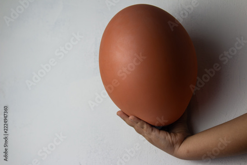 Hand holding a large brown inflated balloon against a white textured wall with copy space on the left