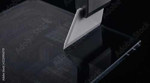 Precision cutting of a microchip using a sharp industrial blade, highlighting intricate electronic pathways and reflective surface