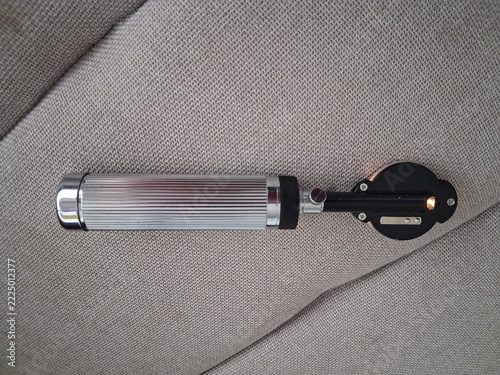 Obraz na plátně Silver and black otoscope medical examination instrument with illuminated viewing head, placed on a gray textured fabric background