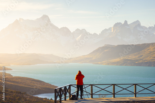 Fotografie View of a photographer with a tripod on a viewing platform overlooking the mountains and lake of Torres del Paine National Park in Magallanes, Chile