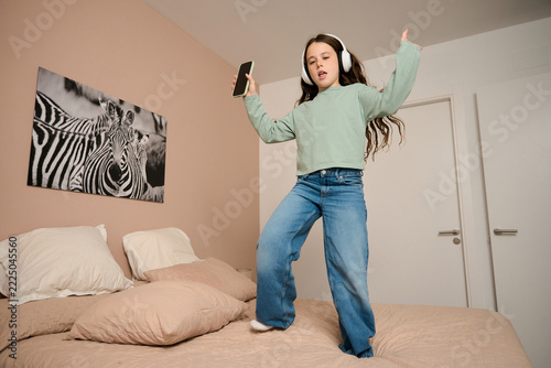 Young girl dancing on bed listening to music