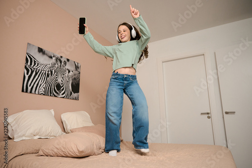 Young girl enjoying music dancing on bed