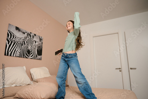 Happy girl jumping on bed listening music