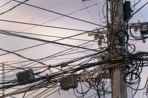 View of a utility pole covered in a dense tangle of electrical and communication wires with attached equipment boxes against a cloudy sky in Mexico.
