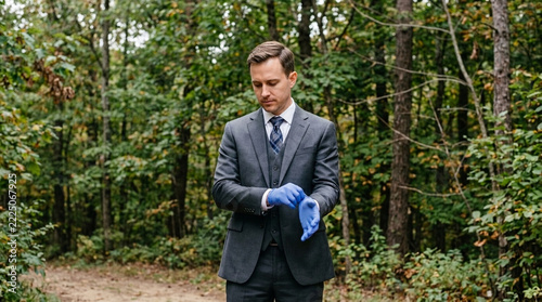 Businessman putting on blue gloves in a forest preparing for outdoor work or exploration