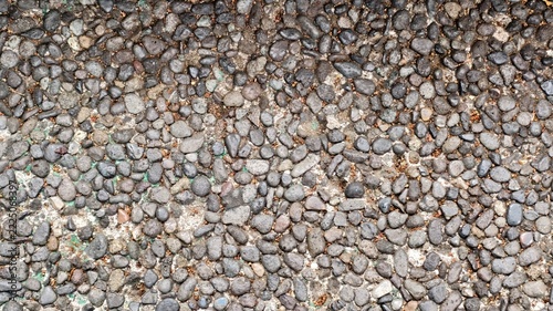 close-up, top-down view of an exposed aggregate concrete surface. It features a dense arrangement of small, rounded river pebbles and stones embedded in a light-colored cement mortar base