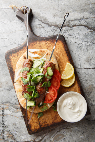 traditional indian minced meat skewers Seekh Kebab with yogurt, naan bread and vegetables closeup on the wooden board. Vertical top view from above