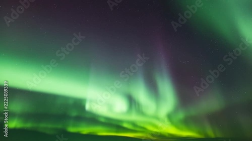 Time lapse pan static aerial view of northern lights swirling and dancing across night sky above arctic horizon with stars