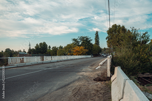 A rural road stretches into the distance, bordered by white railings and lush greenery. The peaceful scene captures the tranquility of a quiet countryside setting.