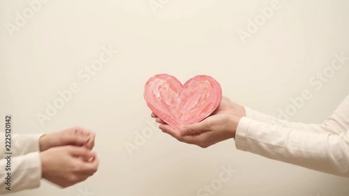 Hands holding a hand painted pink paper heart for love and care