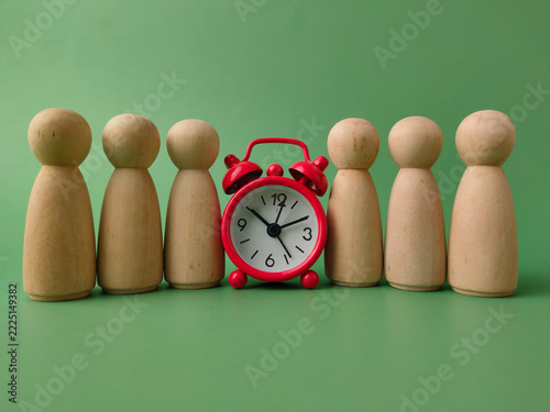 A small red alarm clock sits in the middle of a row of wooden peg dolls