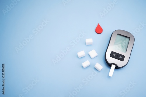 Diabetes concept with blood glucose meter, sugar cubes, blue awareness ribbon and medical gloves on blue background