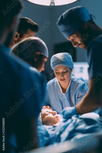 Surgical team performing medical operation on patient in operating room, vertical