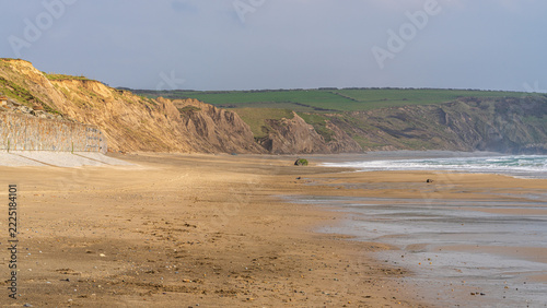 A wide sandy beach with gentle waves, wet sand, and rugged coastal cliffs along the shoreline at Aberdaron on the Llŷn Peninsula in Wales. Calm seaside landscape with open space and soft daylight