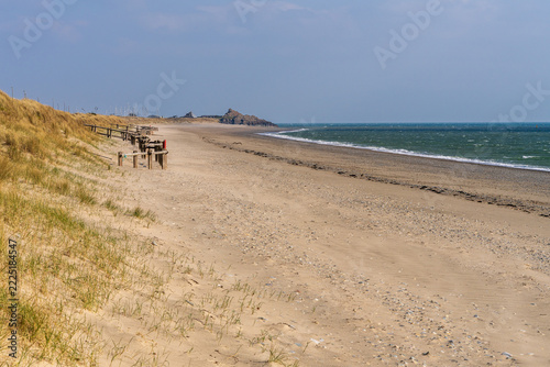 A long sandy beach with coastal dunes, wooden groynes, and choppy sea under clear daylight near Pwllheli on the Llŷn Peninsula. Open coastal landscape with strong leading lines and ample copy space