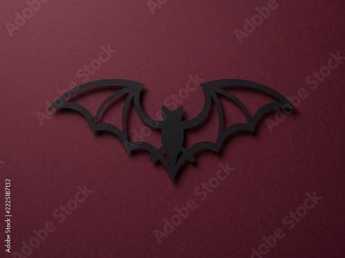 Black paper cut bat with outlined wings and soft shadow on dark red background, horizontal Halloween papercut art