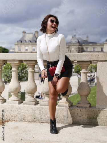 Asian woman in sunglasses leaning against a stone balustrade at a Parisian public park
