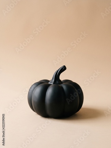 Black matte ceramic pumpkin with long curved stem on peach beige gradient background, vertical copy space