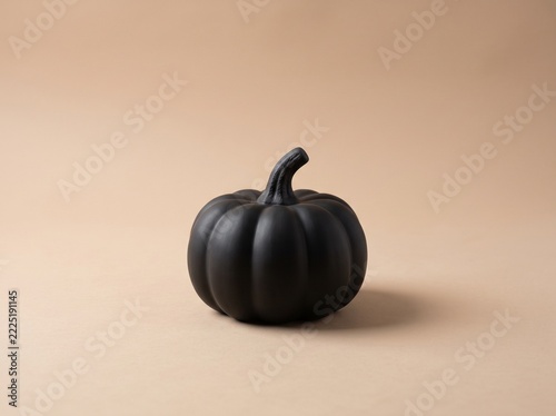 Small matte black ceramic pumpkin on warm beige gradient background, minimalist Halloween decor with copy space