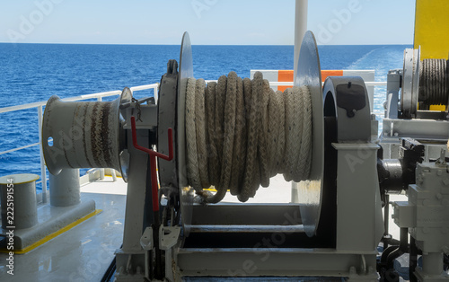 Heavy winch drum wound with thick mooring rope on the deck of a vessel sailing on the open blue sea in Rhodes, Greece.