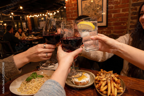Friends Toasting with Red Wine and Lemon Water over Dinner in Cozy Restaurant
