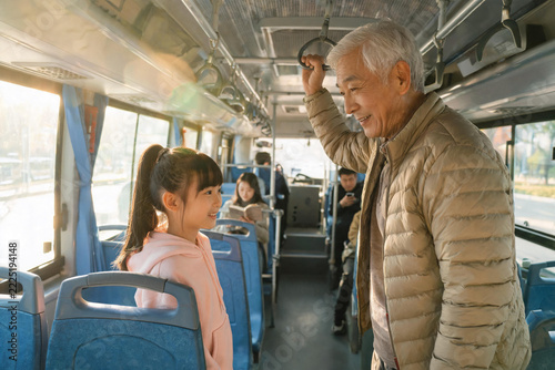 Elderly man and young girl smiling and standing inside a public bus with passengers seated
