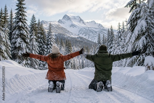 Two people kneeling with outstretched arms on a deeply snow covered forest road