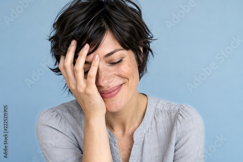 Smiling Woman with Closed Eyes and a Hand across Her Face on Pale Blue