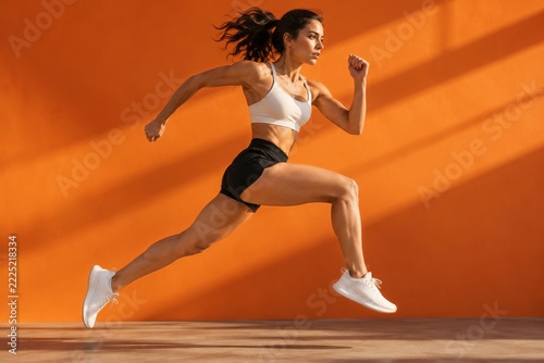 Athletic woman leaping forward in sportswear against a vivid orange background