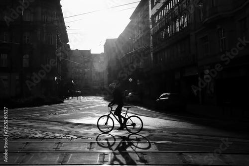 Black and White Urban Street Scene with Cyclist Crossing Tram Tracks in Dramatic Backlight