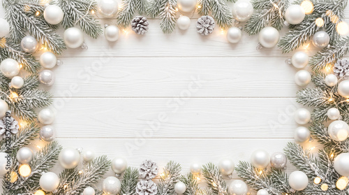 Christmas frame with white ornaments and pine branches on white wooden background
