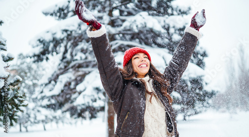 Young woman in winter clothing is having fun in a winter forest. She tosses snow up into the air and enjoys the natural surroundings. A concept of fun, leisure, and the winter season.
