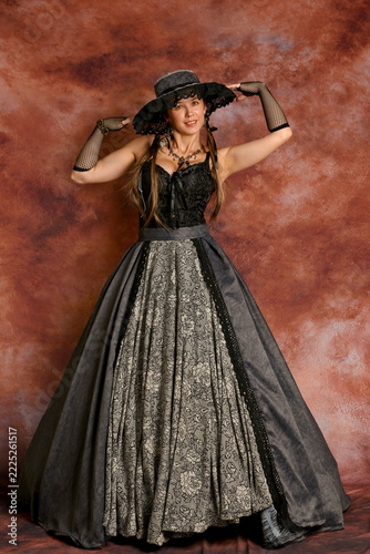 Elegant woman posing in in 19th-century Victorian gown and black hat
