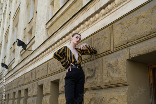 Portrait of an attractive young caucasian woman wearing a yellow and black striped blouse near a building. Looking at camera. Fashion, style, beauty.