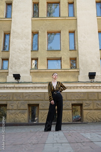 Portrait of an attractive young caucasian woman wearing a yellow and black striped blouse near a building. Looking at camera. Fashion, style, beauty.