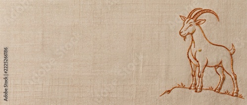 Embroidered goat on textured linen canvas banner with copy space. Handcrafted needlework outline of horned ram