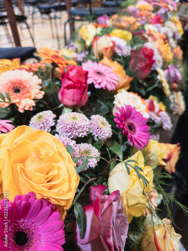 Colorful arrangement of yellow roses, pink gerberas and chrysanthemums in a long floral display in a concert hall with blurred chairs