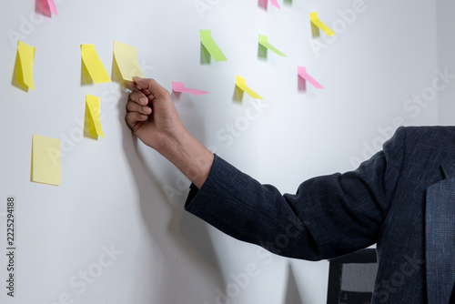 Close-up of a businessman's hand sticking a reminder note on a modern office wall during project planning.