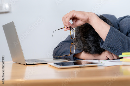 A tired young man falls asleep at his office desk while working on a laptop computer late at night.