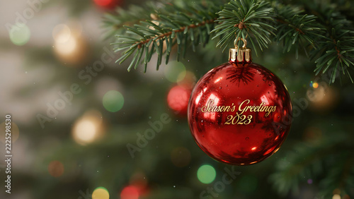 Shiny red christmas bauble hanging from green pine tree branch with golden glowing festive lights in background