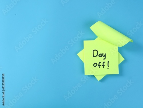 Green adhesive note with handwritten day off text on a bright blue background with copy space. Perfect concept for vacation, office leave, weekend break, holiday, time off, and work life balance