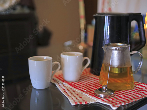 Glass Teapot, black kettle and cups are standing on the table. Food and beverage service with tea brewing equipment and hot drink preparation for welcoming breakfast