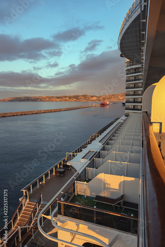Pooldeck or swimmingpool with sun deck on modern cruiseship cruise ship liner in port with sun loungers ready for cruising to Mediterranean on sunny day with city skyline in background