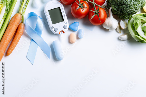 Medical glucose monitor and blue ribbon with fresh tomatoes and greens on white surface for diabetes prevention awareness campaign.