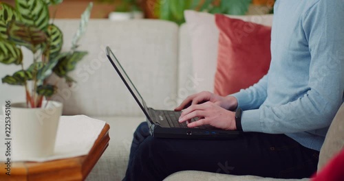 Adult typing on a laptop while seated on a sofa in a bright living room