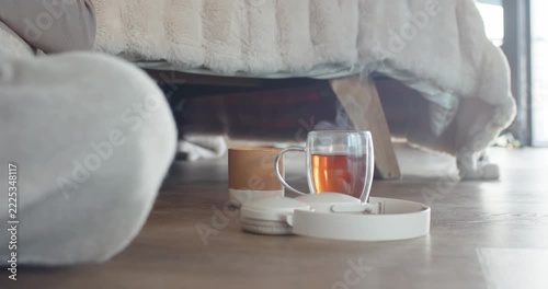 Glass cup is releasing steam as hot tea is cooling on wooden floor beneath bed edge