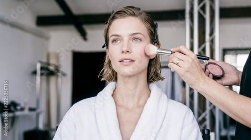 Woman model getting makeup applied by artist backstage