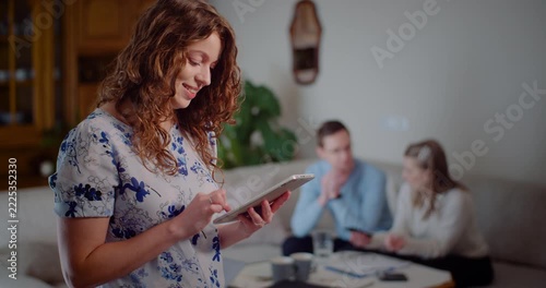 Smiling woman using a tablet in a cozy home living room with people in the background